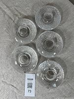 Top-down view of five Orrefors crystal candle holders arranged in a cluster on grey fabric; textured geometric pattern and smooth top surface visible.