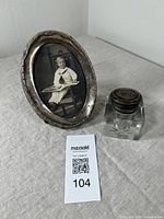 Photo of the antique sterling silver oval picture frame and a sterling lidded inkwell side by side on a table showing overall condition and size.