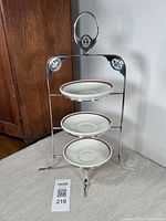 Front view of the antique Victorian silver plated 3-tiered plate stand with the three mid-century saucers displayed on the tiers.