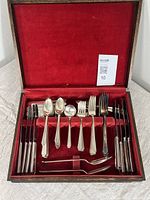 Full view of the open fitted box containing the silver plated cutlery arranged in rows showing knives, forks, spoons and specialty utensils with red velvet lining.