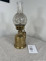 Full view of brass oil lamp with glass chimney on a grey cloth surface, showing overall height and design.