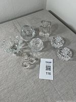 Nine Mid Century Scandinavian style clear glass candle holders arranged on a gray cloth surface showing various shapes and sizes.