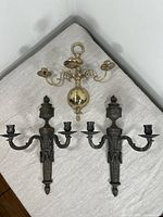 The set of three candle sconces displayed on a light cloth, showing two matching Italian patinated bronze two-arm sconces and one brass three-arm sconce.