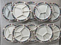 Set of 10 Villeroy & Boch fondue plates arranged on white cloth, displaying the colorful decorative rims and divided plate sections.