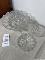 Set of three clear vintage glass bowls with leaf and bubble motifs, one larger and two smaller bowls, arranged on a beige surface against a white wall.