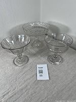 Three antique clear pressed glass footed bowls displayed together on a cloth surface, showing overall size and style.