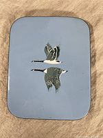 Full front view of the rectangular enamel metal wall art showing the two flying Canadian geese against a light blue background.