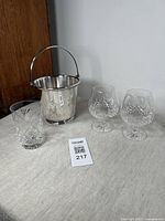 Overall view of the silver plate ice bucket, two Galway crystal snifters and one tumbler on a linen cloth surface.
