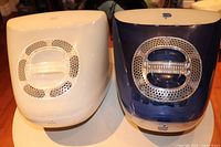 Two vintage iMac G3 computers shown from rear, highlighting blue and white translucent plastic egg-shaped cases with circular ventilation grilles.