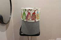 Photo showing two lampshades stacked, top one with colorful bird print and bottom one grey fabric.