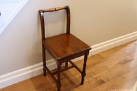 Antique wooden vanity chair showing front and side profile with turned legs and wooden seat under natural lighting.