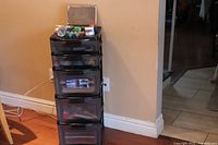 Tall black 5-drawer storage chest in corner of room with various small art supplies on top.