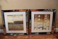 Two large square abstract pictures side by side with beveled mirror frames, one with circular patterns and one with gradient style landscape. Both approximately 28x28 inches.