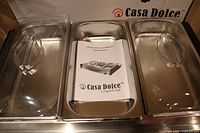 Top view showing three large clear-lid removable trays and an instruction manual inside the center tray.