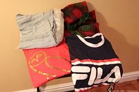 Red owl t-shirt, blue FILA t-shirt, light baby jumpsuit, and grey scarf folded on the floor