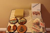 Overall set including 4 Da Luisa wooden coasters on table, stack of Native Indian coasters with box, and pile of fabric drawer sachets