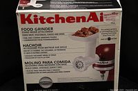 Box front showing KitchenAid branding and image of the food grinder attachment with description of features.