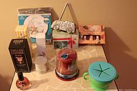 Photo shows the lot with English Leather Black cologne in box, JAM Bluetooth speaker, basket with green silicone lid, an angel decorative plaque, a white jar, and some other small items.