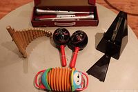 Lot of musical instruments including pan flute, maracas, toy accordion and metal metronome on table