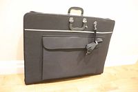 Closed view of new black art portfolio case showing handle, shoulder strap, and outer pocket with velcro flap