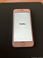 Apple iPhone 6s smartphone powered on showing 'Hello' setup screen, placed on a flat dark surface.