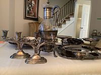 Photo showing two small plated double candleholders and a glass decanter with a silver-tone holder with handle on a table in a home setting.