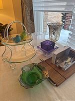 Wide shot of 10 pieces including serving stand, green glass bowl, vase, containers, cutting board with utensils, and bird figurines