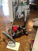 Full view of Dyson DC32 canister vacuum with hose and wand attached, positioned on hardwood floor with surrounding indoor furniture