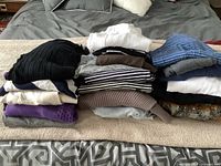 20 assorted ladies sweaters in multiple colors and patterns folded in stacks on bed.