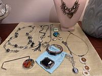 Over 10 pieces of vintage silver-tone and enamel jewelry including necklaces, bracelets, and brooches arranged on a beige surface.