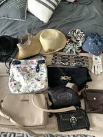 Lot of over 10 vintage purses and hats arranged on a bed, showing variety including floral prints, black purses, and several hats along with a pair of gloves