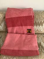 View of one folded pink and dark pink wool blanket featuring horizontal stripes and a Witney Point sewn-on label.