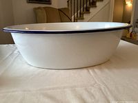 Side angle showing the large oval shape with white enamel and dark blue rim on the edge. Some scratches and marks visible on the base indicating wear.