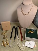 Photo showing the full lot of 6 vintage jewelry pieces including necklaces displayed on a bust, earrings, and the Swarovski brooch in the original box with paperwork.
