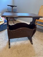 Front angled view of the vintage solid wood side table showing top surface and magazine holder base with carved detail.