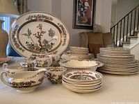 Overview of dinnerware set showing large oval serving platter at back with stacked plates, bowls, cups, saucers and serving pieces.