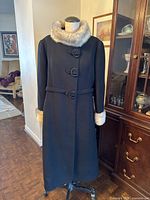 Full view of the black wool vintage coat on a dress form showing fur collar and cuff trims and full length fall