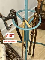 Four vintage wooden walking sticks displayed in a metal stand, various carved handles including an animal-shaped handle