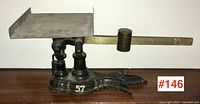 Side view of antique Fairbanks balance scale showing black cast iron base with number '57', metal platform and brass sliding weight.
