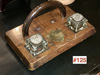 Top and angled view of antique oak ink stand showing curved handle, glass ink bottles with decorative lids, and brass shield on wooden base.