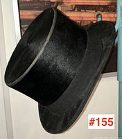 Black antique top hat hanging on a turquoise metal rack, showing profile and shape.