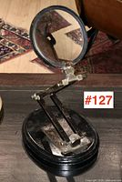 Magnifying glass with 4-inch diameter lens mounted on articulated arm on black oval base with some surface wear visible.