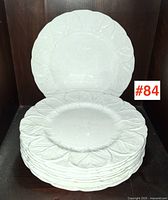 Stack of eight white dinner plates with embossed leaf pattern against dark background