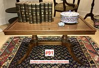 Front view of the walnut coffee table on a patterned rug with some decorative items on top (not included in lot). The table has carved edges and sturdy pedestal legs ending in brass claw feet.