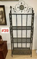 Front view of vintage folding bakers shelf showing full height and metal lattice shelves with decorative scrollwork and motifs on top backrest.