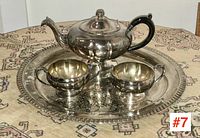 Vintage silver plate tea set with teapot, sugar bowl, creamer on ornate round tray on patterned fabric