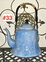 Front view of vintage blue and white spatterware aluminium teapot with curved spout and curved black handle wrapped in natural material for grip.
