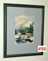 Framed watercolour painting with snowy mountains, trees, and a stream with gray mat and black frame, shown front view.