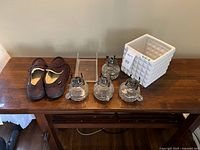 Full lot view showing four antique glass lanterns with metal tops, white ceramic planter, and brown men's slippers on wooden table.