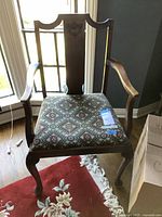 Front view of antique wooden chair showing upholstered seat with patterned fabric, curved arms, and cabriole legs